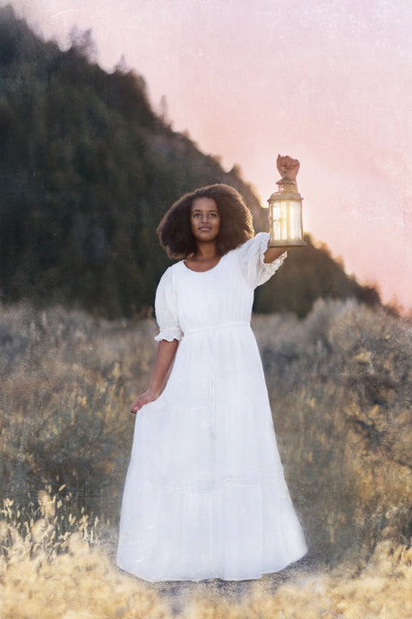 A woman in a white dress holds up a lantern.