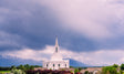 The Orem Utah Temple with a cloudy blue sky and mountains.